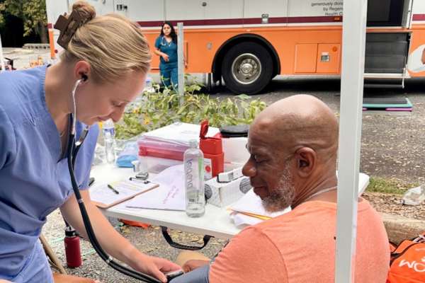 A clinician checks a man's blood pressure at an outdoor community event.