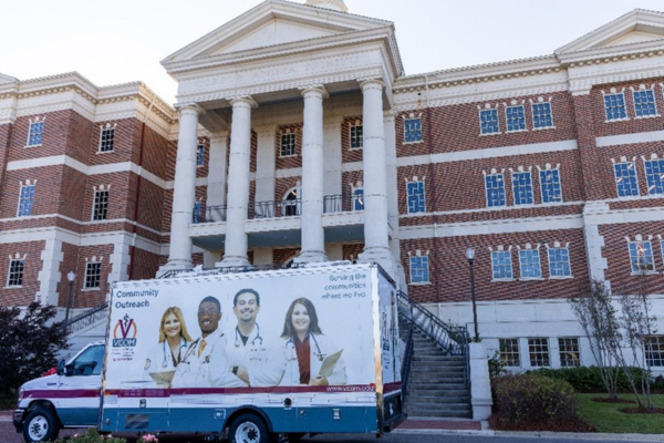 A colorful community outreach truck is parked in front of a grand, red-brick building with tall white columns.